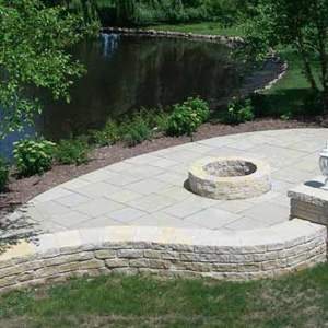 OUTDOOR LANDSCAPE FIRE PIT WITH A SEATWALL & PILLARS ALONG POND